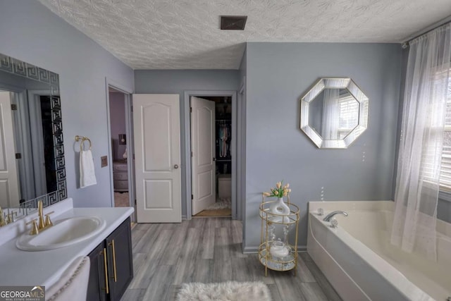 bathroom featuring a tub to relax in, a textured ceiling, wood-type flooring, and vanity