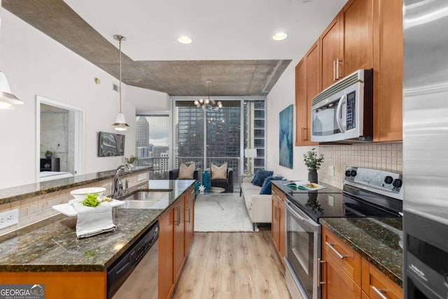 kitchen featuring appliances with stainless steel finishes, decorative light fixtures, an island with sink, sink, and dark stone countertops