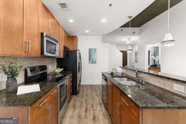 kitchen featuring sink, light hardwood / wood-style flooring, appliances with stainless steel finishes, dark stone countertops, and hanging light fixtures