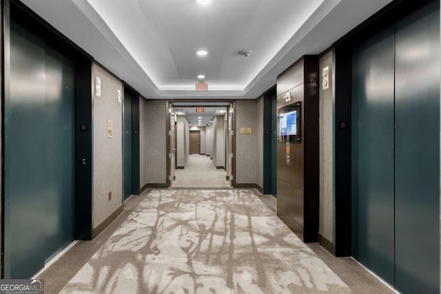 corridor featuring a raised ceiling, light carpet, and elevator