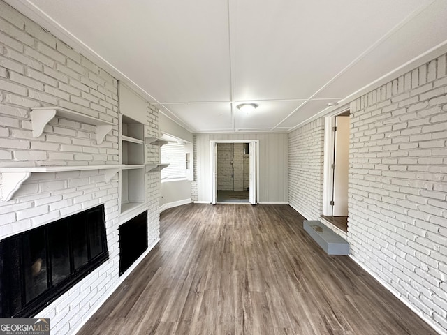 unfurnished living room with dark hardwood / wood-style floors, brick wall, and a fireplace