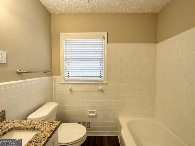 bathroom with tile walls, vanity, a textured ceiling, a tub, and toilet