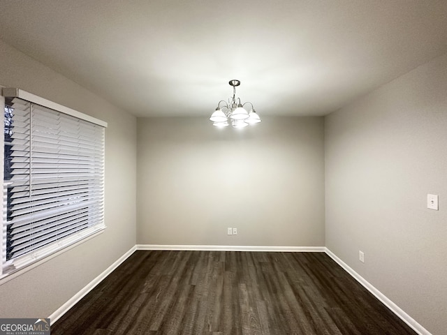 empty room with a notable chandelier and dark wood-type flooring