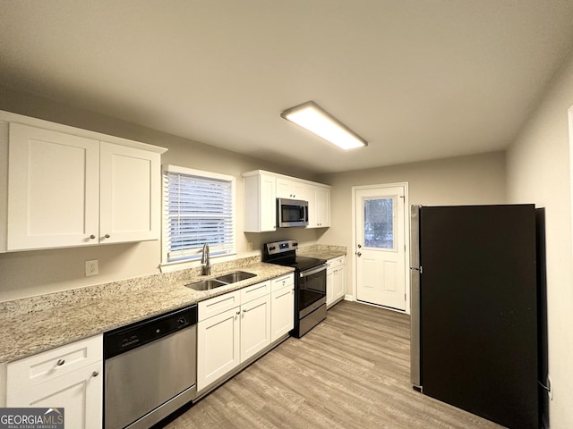 kitchen with sink, stainless steel appliances, light stone countertops, white cabinets, and light wood-type flooring