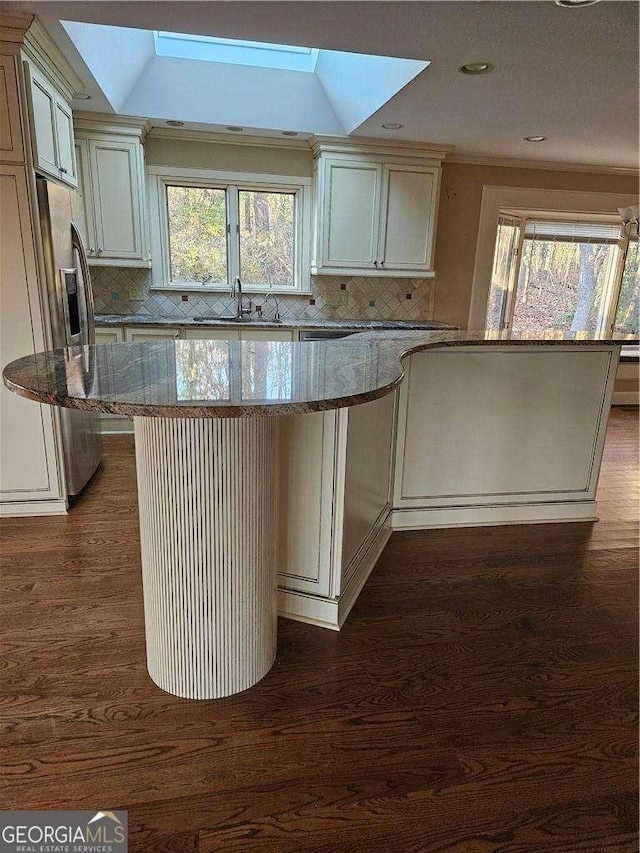 kitchen featuring dark wood-type flooring, sink, light stone counters, a kitchen island, and decorative backsplash