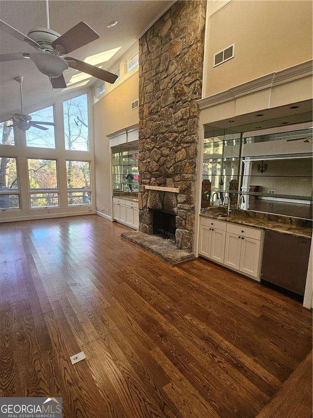 unfurnished living room featuring dark hardwood / wood-style floors, ceiling fan, a stone fireplace, and high vaulted ceiling