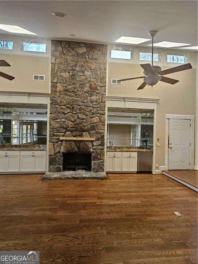 unfurnished living room featuring a towering ceiling, dark wood-type flooring, a fireplace, and ceiling fan