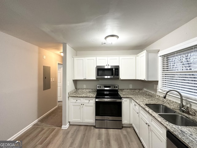 kitchen with sink, appliances with stainless steel finishes, white cabinetry, light stone countertops, and light wood-type flooring