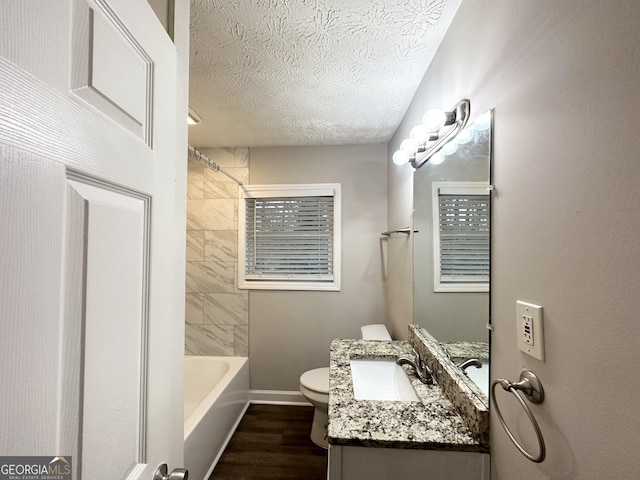 full bathroom with tiled shower / bath combo, vanity, wood-type flooring, a textured ceiling, and toilet