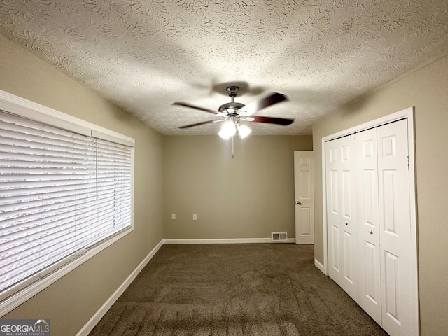 unfurnished bedroom with ceiling fan, a textured ceiling, dark carpet, and a closet