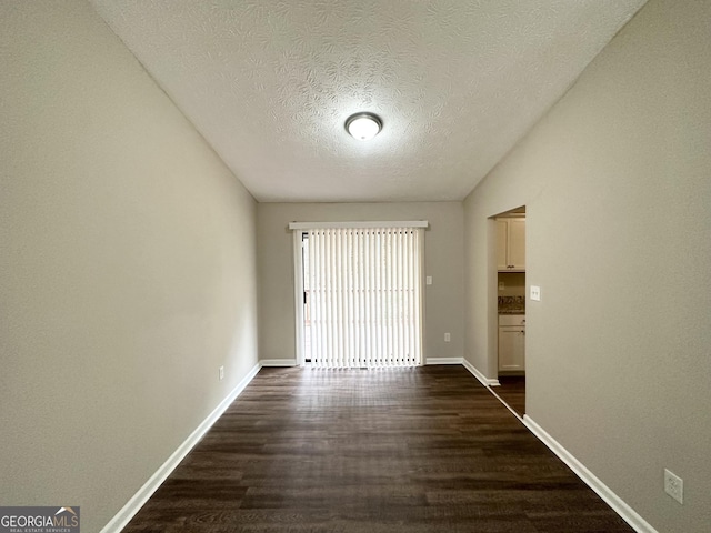 unfurnished room featuring lofted ceiling, dark hardwood / wood-style floors, and a textured ceiling