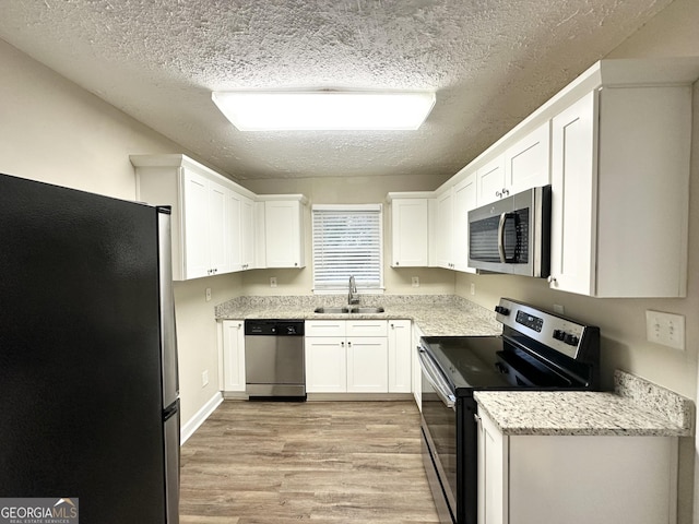 kitchen with sink, white cabinetry, a textured ceiling, stainless steel appliances, and light hardwood / wood-style floors