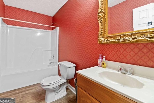 full bathroom with toilet,  shower combination, wood-type flooring, a textured ceiling, and vanity