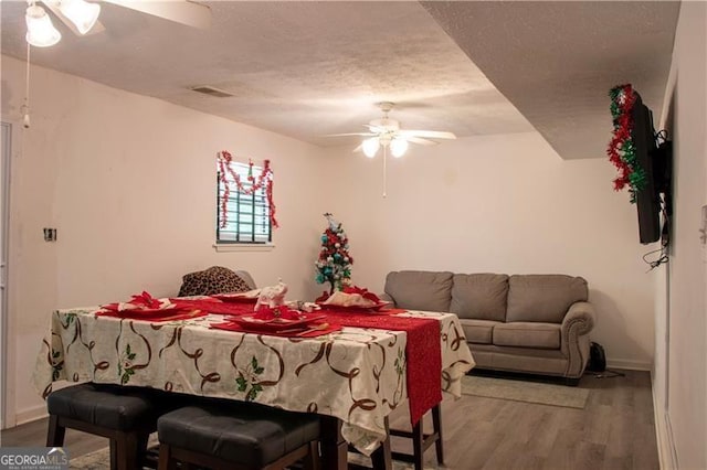 living room with visible vents, ceiling fan, a textured ceiling, wood finished floors, and baseboards