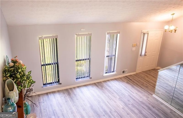 empty room with visible vents, baseboards, wood finished floors, an inviting chandelier, and a textured ceiling