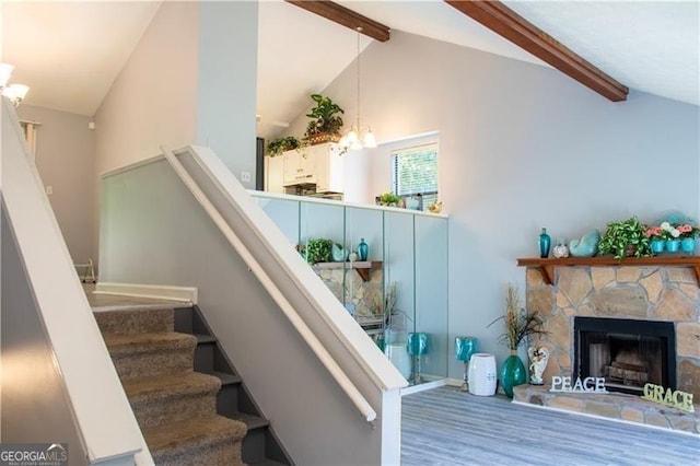 staircase with a chandelier, wood finished floors, beamed ceiling, a stone fireplace, and high vaulted ceiling