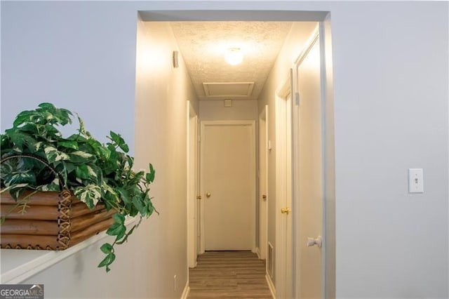 hallway featuring attic access, light wood-style floors, and baseboards