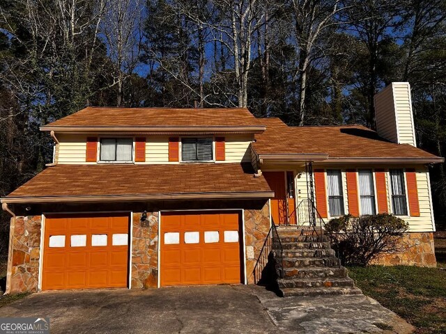 split level home with stone siding, a chimney, an attached garage, and driveway