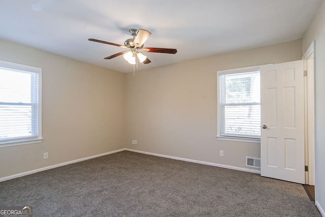 spare room featuring dark colored carpet, ceiling fan, and a wealth of natural light