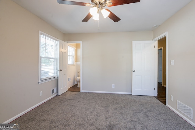 unfurnished bedroom featuring ceiling fan, ensuite bathroom, and dark carpet