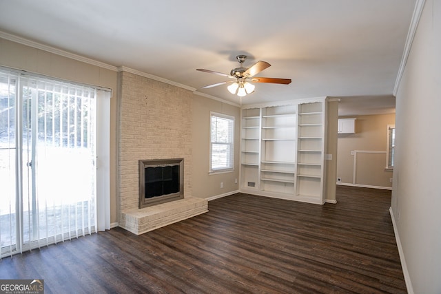 unfurnished living room with built in features, ceiling fan, crown molding, a brick fireplace, and dark wood-type flooring