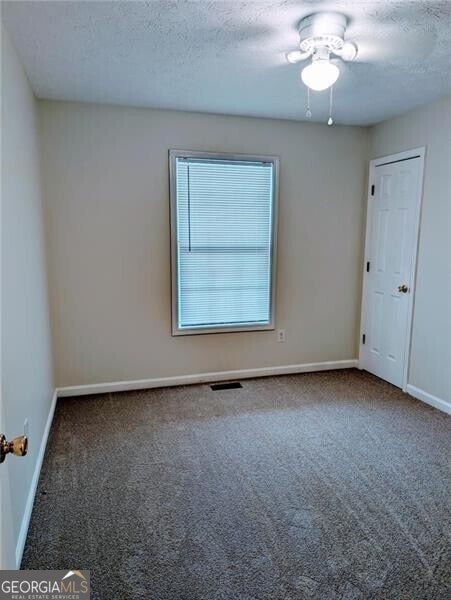 unfurnished room featuring a textured ceiling and dark colored carpet