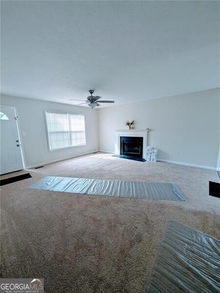 unfurnished living room featuring ceiling fan and carpet floors