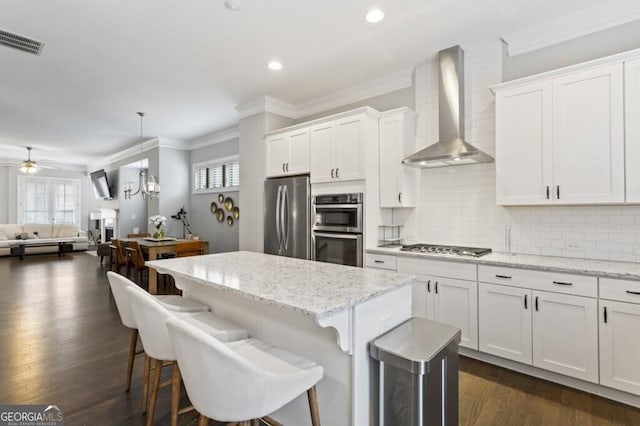 kitchen with wall chimney range hood, a kitchen breakfast bar, a kitchen island, stainless steel appliances, and white cabinets