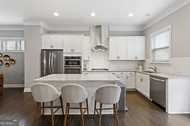 kitchen featuring white cabinets, a center island, wall chimney exhaust hood, and appliances with stainless steel finishes