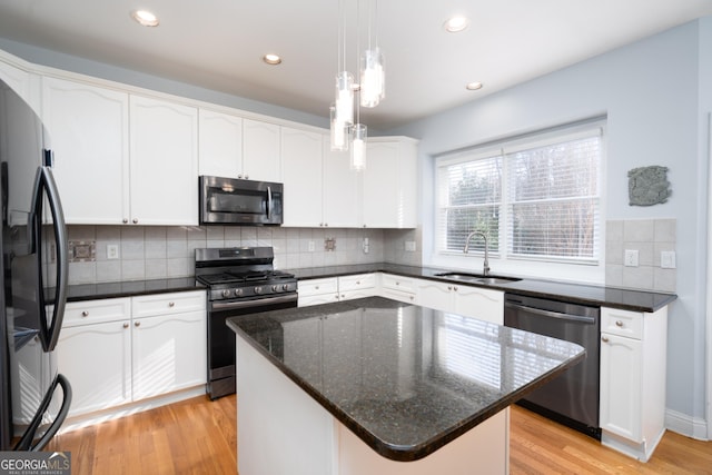 kitchen with appliances with stainless steel finishes, sink, white cabinetry, a kitchen island, and decorative light fixtures