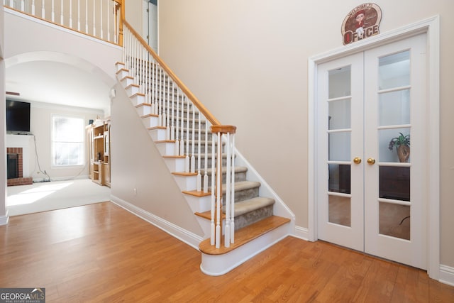 stairs featuring a high ceiling, french doors, hardwood / wood-style floors, and a brick fireplace