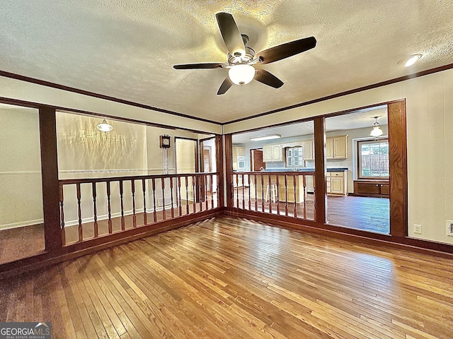 empty room with wood-type flooring, ornamental molding, ceiling fan, and a textured ceiling