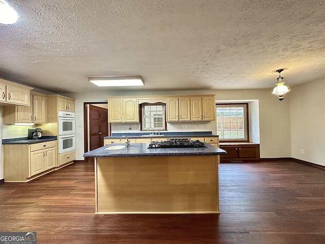 kitchen with pendant lighting, sink, double oven, an island with sink, and light brown cabinets