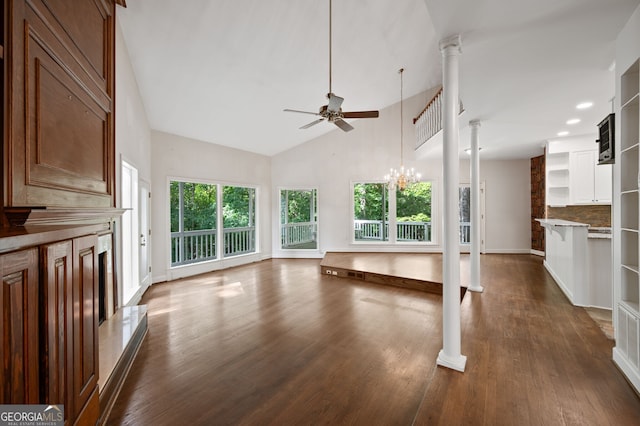 unfurnished living room with ceiling fan with notable chandelier, dark hardwood / wood-style floors, high vaulted ceiling, and ornate columns