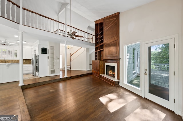 unfurnished living room featuring ornate columns, a towering ceiling, a large fireplace, dark hardwood / wood-style flooring, and ceiling fan