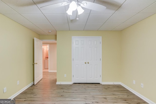 unfurnished bedroom featuring a drop ceiling, a closet, and light wood-type flooring