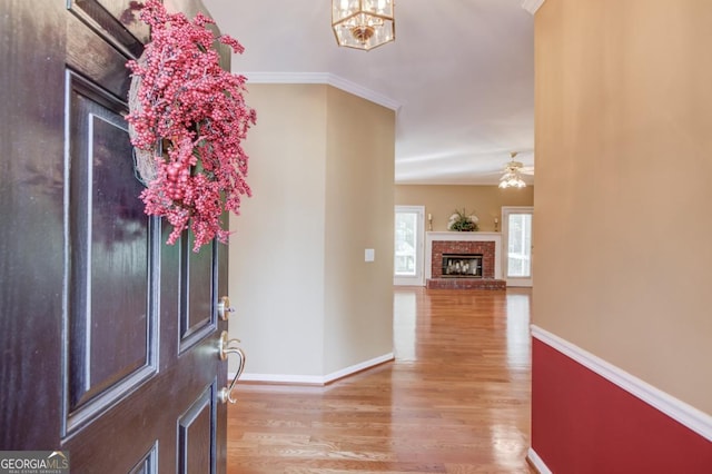 entrance foyer featuring crown molding, ceiling fan with notable chandelier, hardwood / wood-style floors, and a brick fireplace