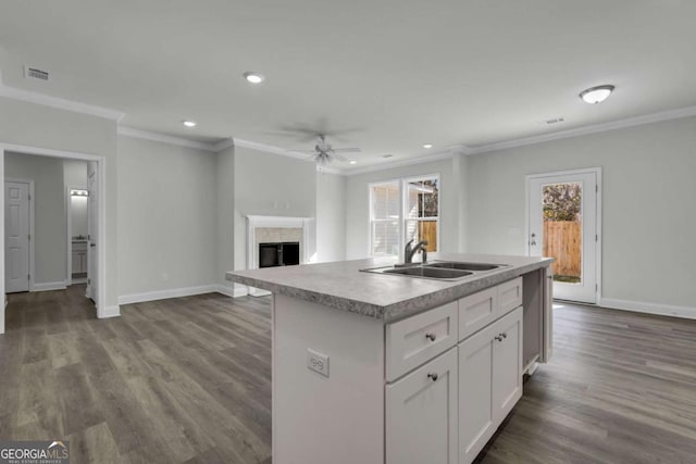 kitchen featuring a tile fireplace, an island with sink, sink, white cabinets, and crown molding