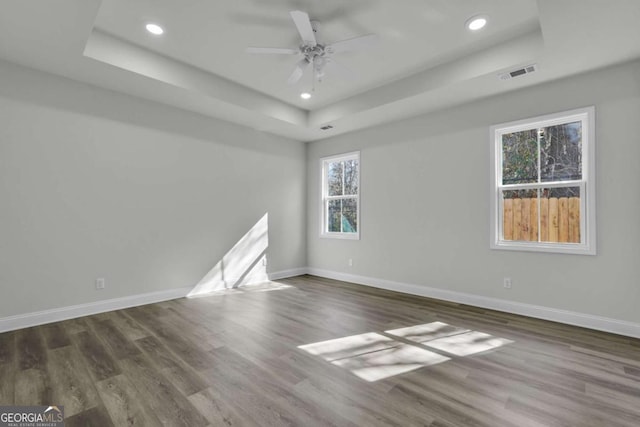 empty room with dark hardwood / wood-style flooring, a raised ceiling, and ceiling fan