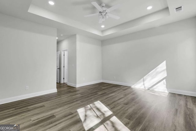 empty room featuring dark hardwood / wood-style floors, ceiling fan, and a tray ceiling