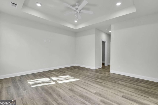 empty room with ceiling fan, wood-type flooring, and a raised ceiling