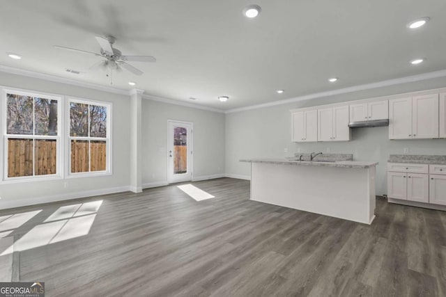 kitchen with light stone counters, a center island with sink, ornamental molding, hardwood / wood-style flooring, and white cabinets