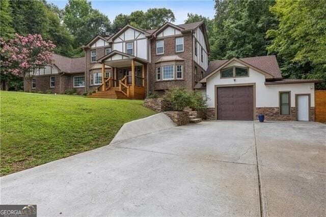 tudor-style house featuring a garage, concrete driveway, and a front yard