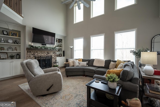 living room featuring dark wood-type flooring, ceiling fan, plenty of natural light, and a brick fireplace