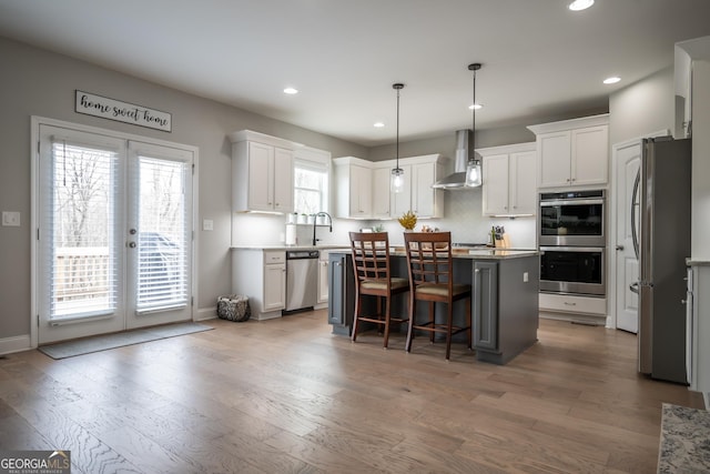 kitchen with pendant lighting, wall chimney range hood, stainless steel appliances, a center island, and white cabinets