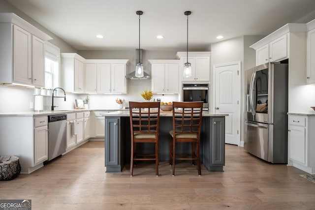 kitchen featuring white cabinetry, a center island, hanging light fixtures, appliances with stainless steel finishes, and wall chimney range hood