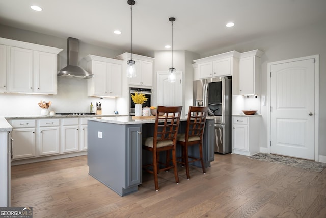 kitchen with a kitchen island, white cabinetry, hanging light fixtures, stainless steel appliances, and wall chimney exhaust hood