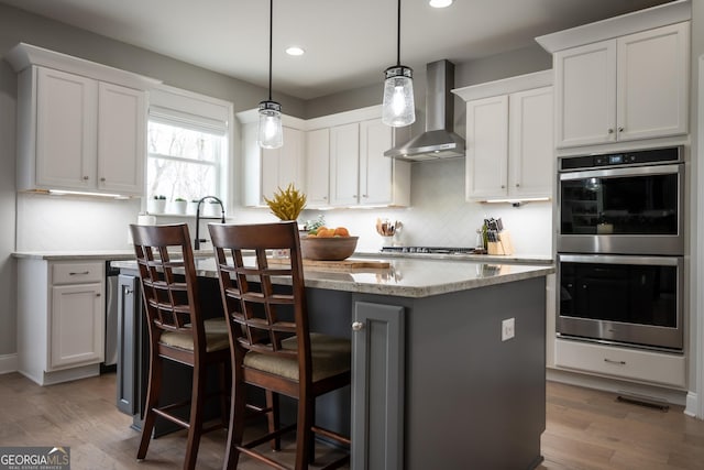 kitchen with wall chimney range hood, stainless steel appliances, white cabinets, and a kitchen island