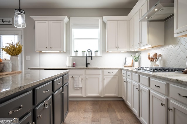 kitchen featuring stainless steel gas cooktop, light stone counters, hanging light fixtures, wall chimney range hood, and white cabinets