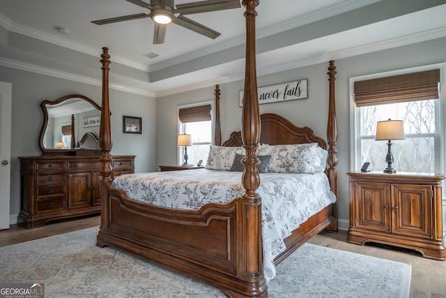 bedroom with crown molding, light hardwood / wood-style floors, a raised ceiling, and ceiling fan